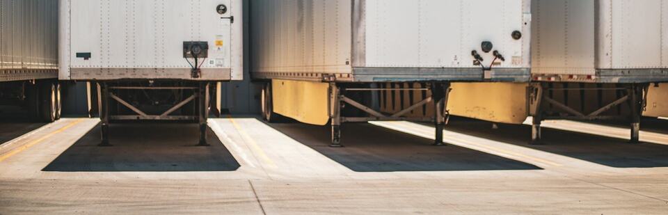 Row of dry van trailers backed into warehouse loading docks with long afternoon shadows