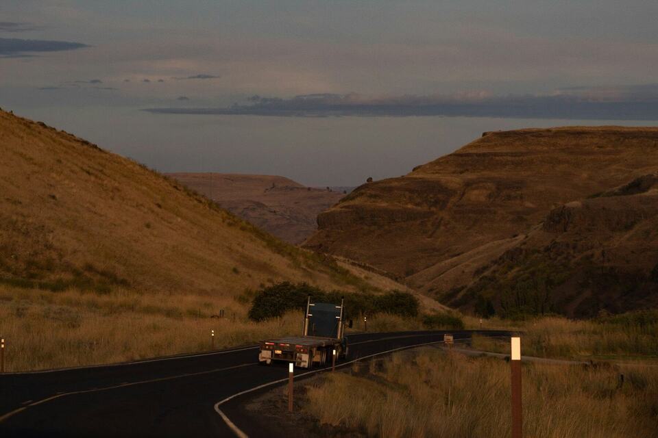 A tractor-trailer rounding a curve on a two-lane road through hills at dusk