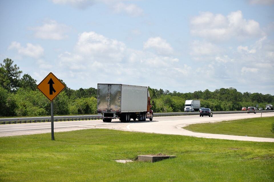 A dry van trailer merging onto a divided highway under a bright sky
