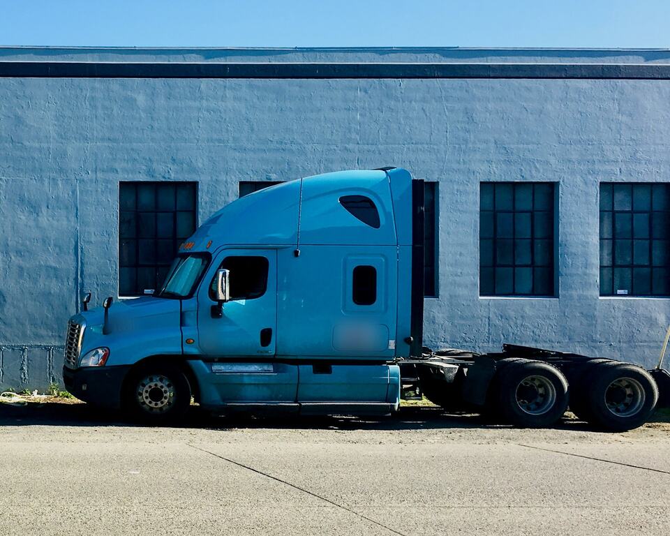 A blue sleeper-cab semi tractor parked beside a painted warehouse wall