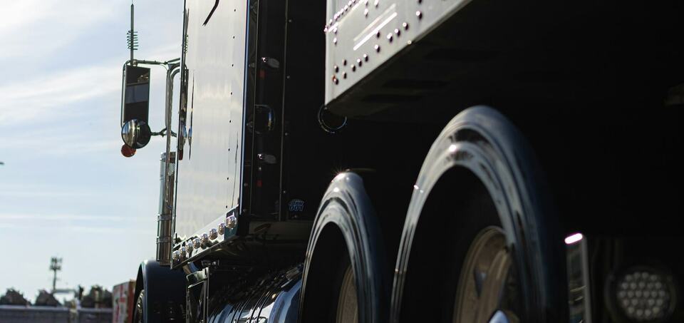 Close-up of a semi truck's polished trailer and tandem wheels in afternoon light